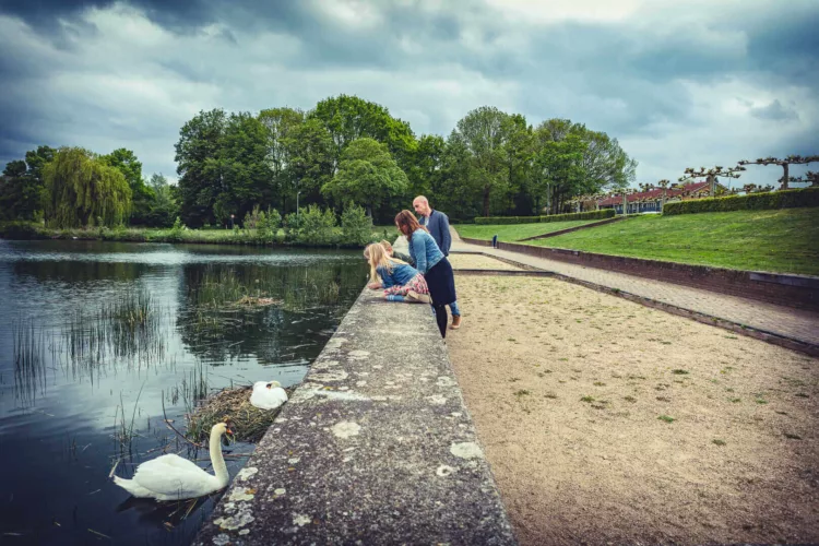 Een gezin met twee volwassenen en twee kinderen bij een waterkant met zwanen in de buurt.