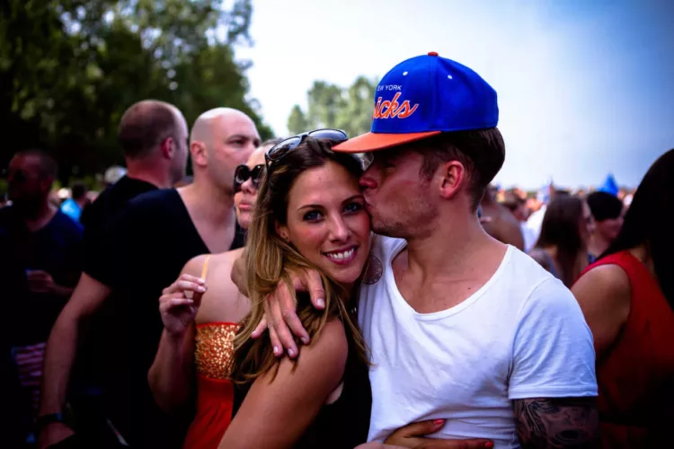 Een man kust een vrouw op de wang terwijl ze samen op een festival staan.