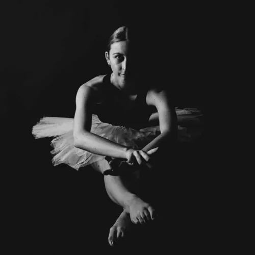 Balletdanseres zittend met een tutu in een zwart-witte afbeelding met schaduw.