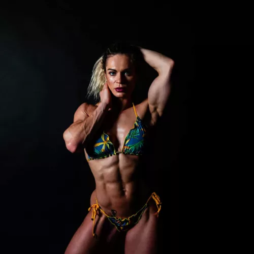 Vrouw met een atletisch figuur in een bikini met een tropisch patroon, poseert met een hand in het haar.