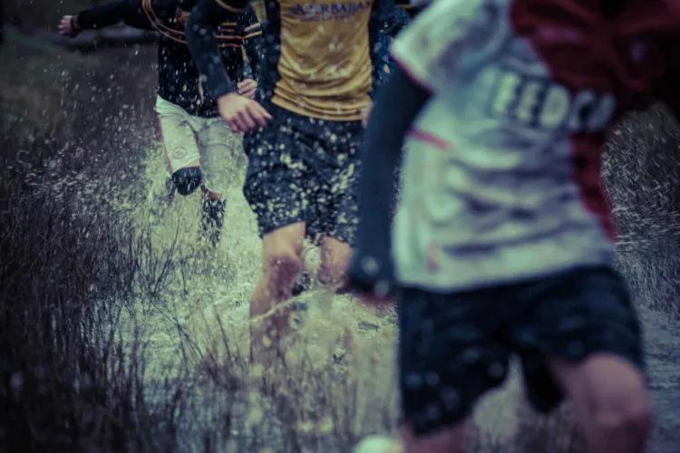 Groep hardlopers die door een modderige plas water rennen tijdens een training in de regen.
