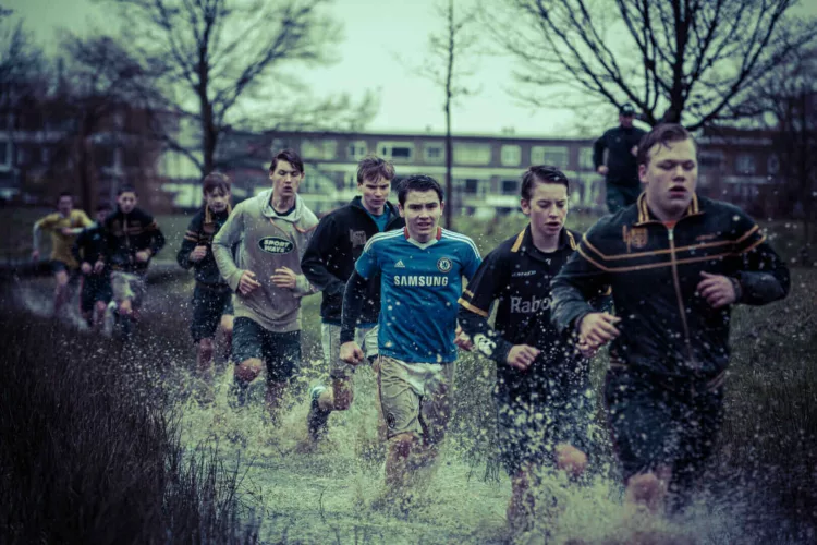 Groep jongeren in sportkleding die door een grote plas water rennen tijdens een training.