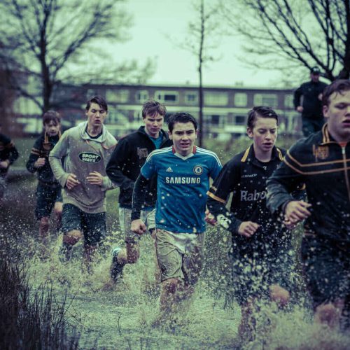 Groep jongeren in sportkleding die door een grote plas water rennen tijdens een training.
