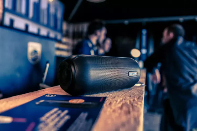 Zwarte Philips soundbar geplaatst op een houten oppervlak met mensen op de achtergrond.