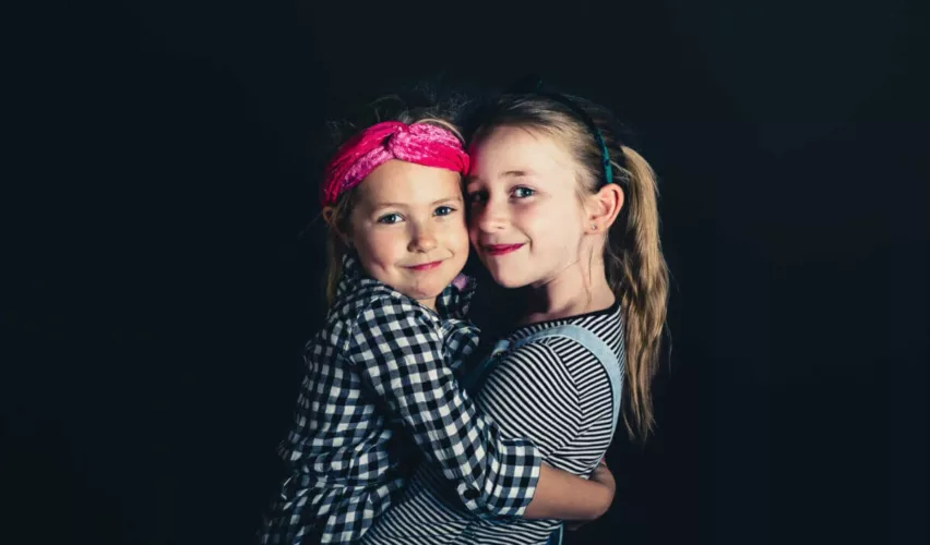 Twee meisjes met verschillende kledingstijlen die elkaar omarmen en naar de camera kijken.