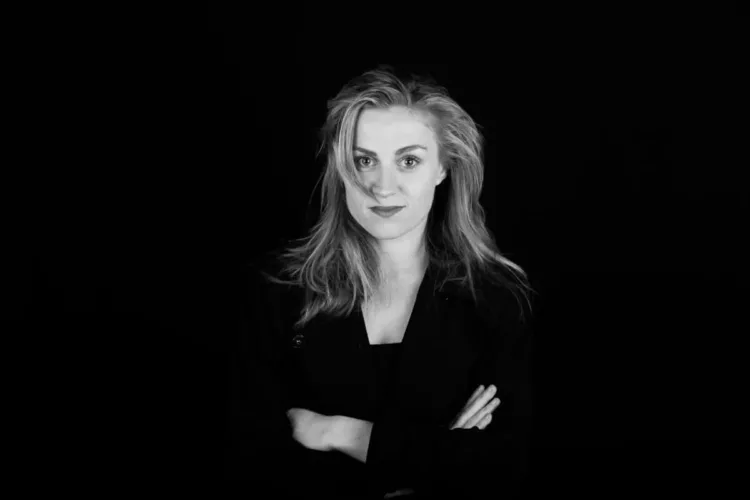 Zwart-wit portret van een vrouw met los haar en een neutrale uitdrukking, armen over elkaar.
