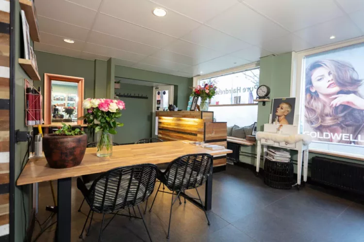 Interieur van een kapsalon met een houten tafel en een vaas met bloemen op de tafel.