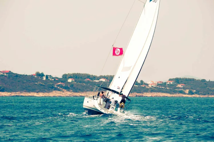 Een zeilboot met witte zeilen vaart over het water, met een vlag aan de mast.
