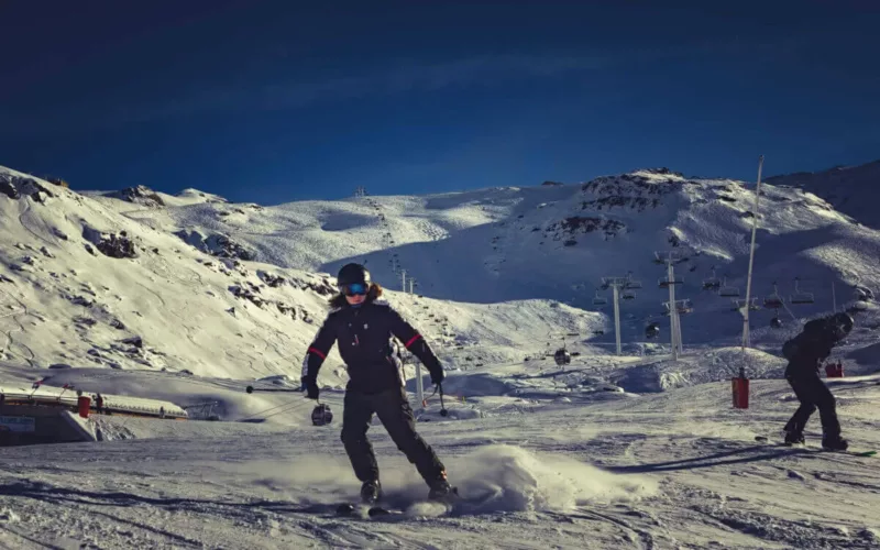 Skiër die over een besneeuwde helling glijdt met bergen op de achtergrond.