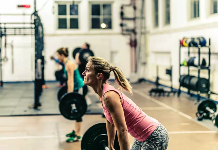 Vrouw met een roze shirt die een deadlift uitvoert met een halter in een sportschoolomgeving.