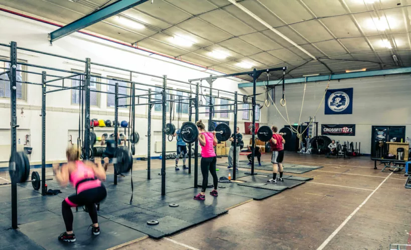 Drie sporters die halters tillen in een Crossfit trainingsruimte met verschillende fitnessapparaten.