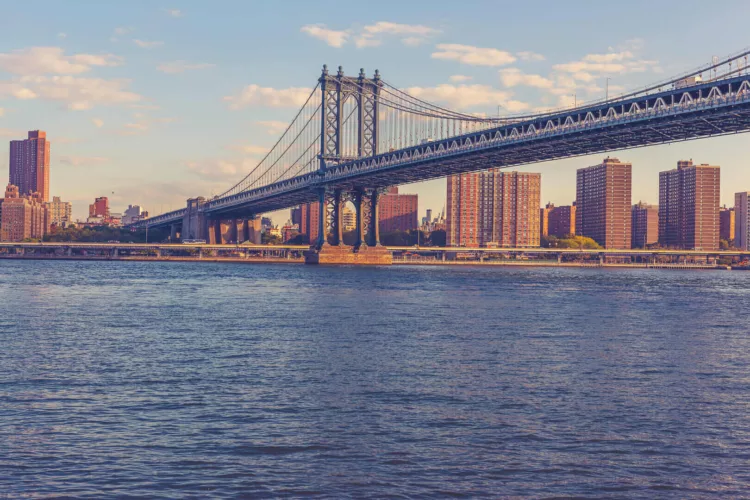 De Brooklyn Bridge met de skyline van New York op de achtergrond en een reflectie in het water.