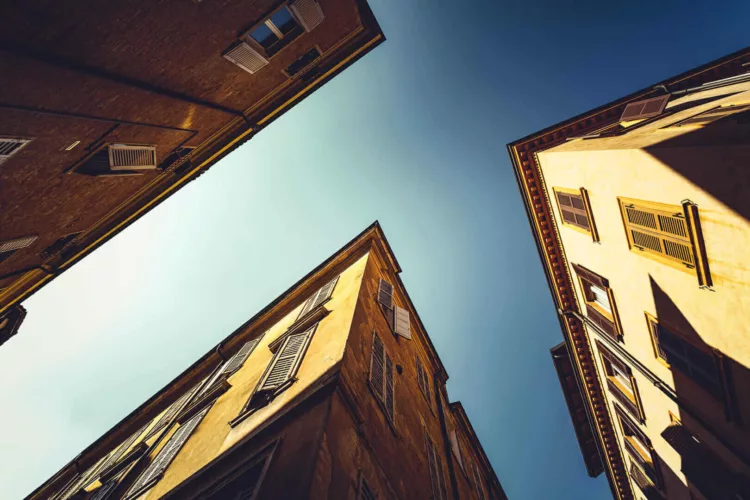 Uitzicht naar de lucht tussen twee gebouwen met gele gevels en vensters in Modena, Italië.