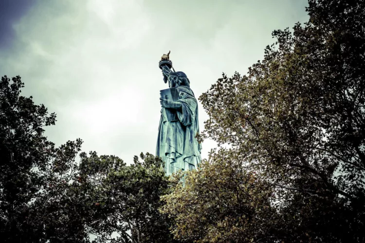 Standbeeld van de Vrijheid zichtbaar tussen bomen in New York, met de fakkel omhoog geheven.