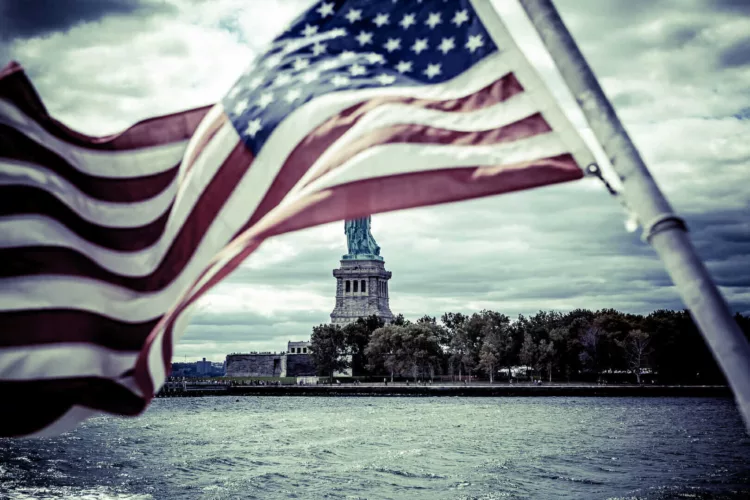 Amerikaanse vlag met het Standbeeld van de Vrijheid op de achtergrond, zichtbaar vanaf het water.