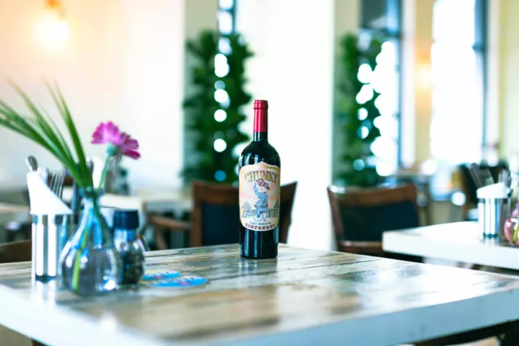 Een fles rode wijn met een etiket op een houten tafel in een restaurantomgeving.