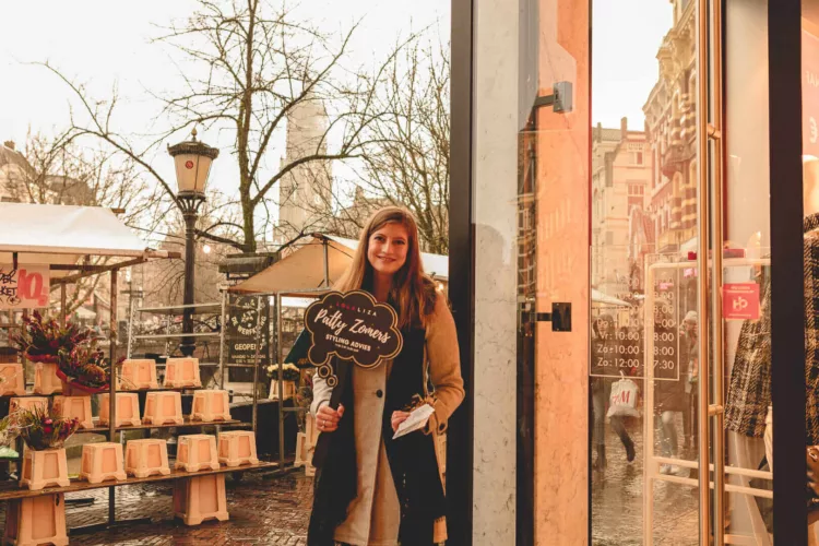 Vrouw die een bord vasthoudt met de tekst 'Patty Zomers' voor een winkel in Utrecht.