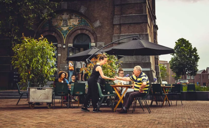 Een serveerster brengt een gerecht naar een klant aan een tafel op het terras van een café.