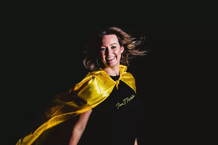 Vrouw met een gele cape en een zwarte T-shirt, lachend met wapperend haar.
