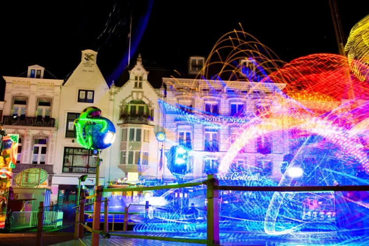 Kermis in Den Bosch met kleurrijke lichten en attracties op een nachtelijke achtergrond.