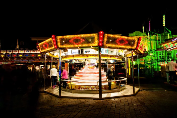 Draaimolen met kleurrijke verlichting en bezoekers op een kermis in de avond.