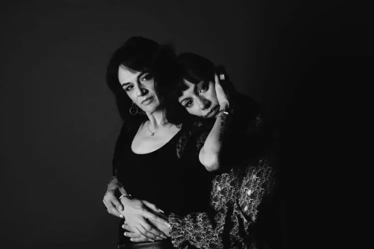 Twee vrouwen poseren samen in een zwart-wit portret met een donkere achtergrond.