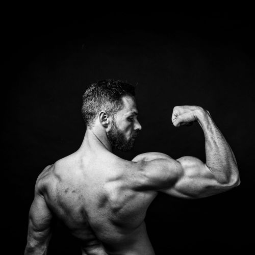 Man met een gespierde arm die naar zijn biceps kijkt in een zwart-wit afbeelding.