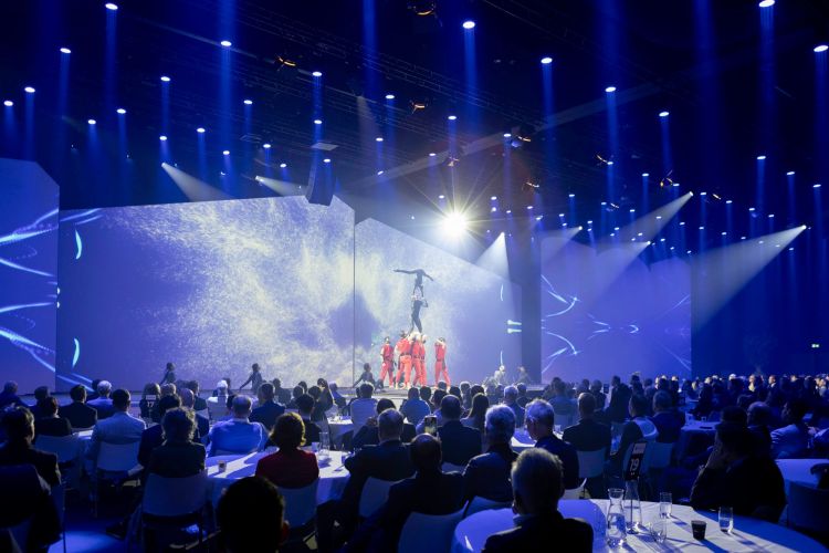 Een podium met een lichtshow en performers tijdens een evenement voor een groot publiek.