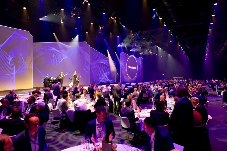 Een evenement met muzikale optredens en een dinersetting in een grote zaal met verlichting.