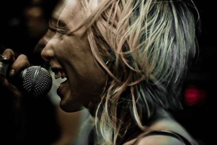 Zangeres met blond haar die in een microfoon zingt tijdens een live optreden.