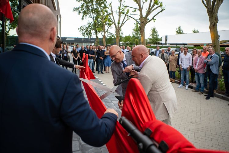Mannen knippen een rood lint tijdens een openingsevenement met een schaar.