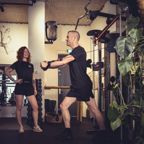 Man die een fitnessoefening uitvoert met een vrouw die toekijkt in een sportschool.
